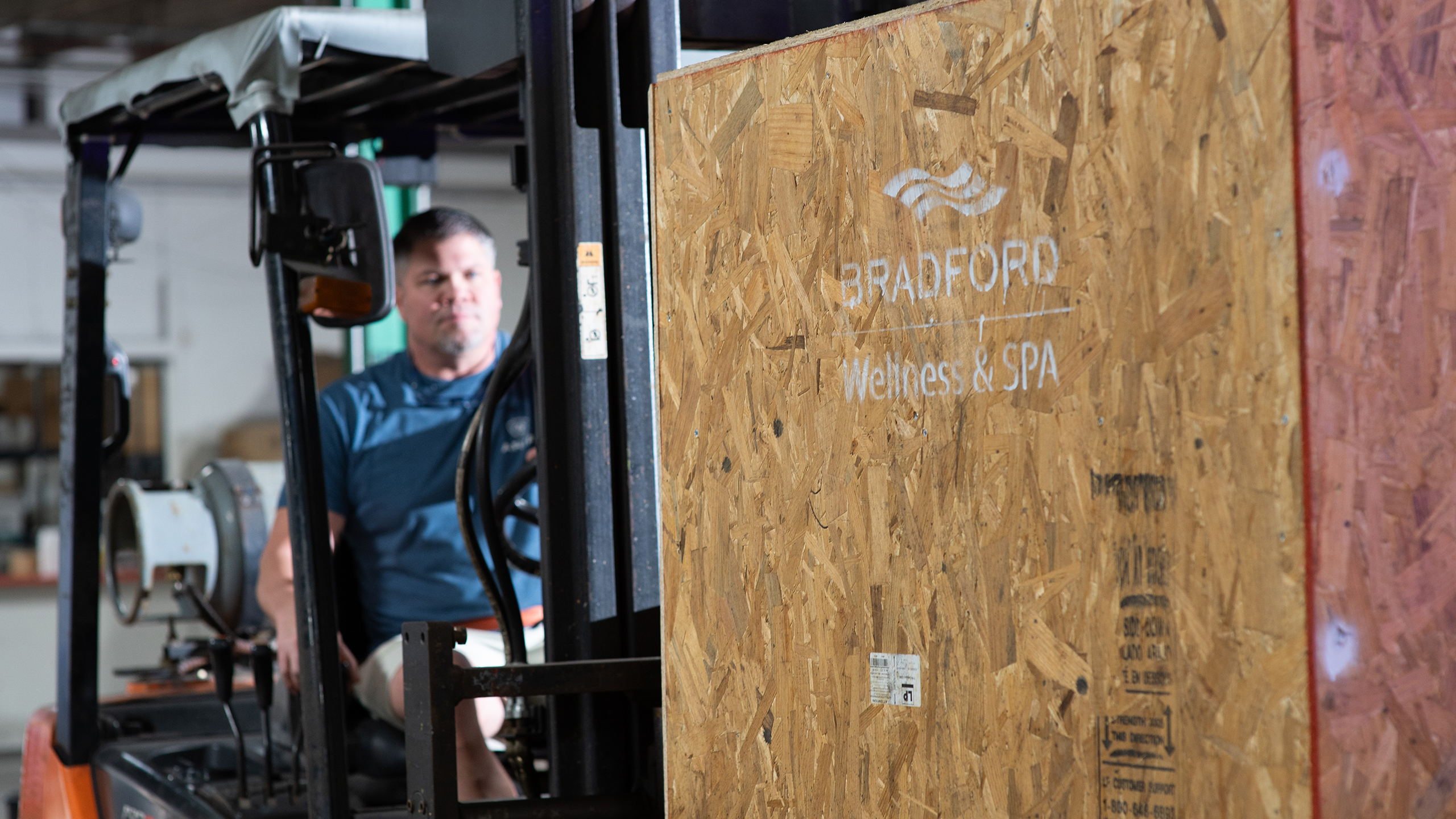 Forklift operator carrying a Bradford Wellness & Spa crate